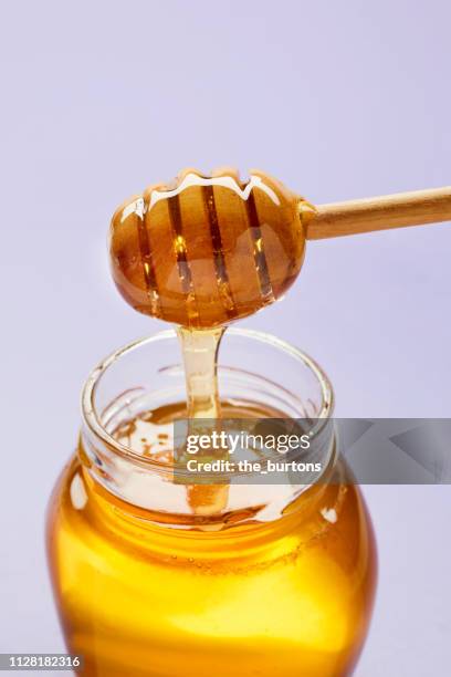 honey dipper with liquid honey in jar on purple background - honey dipper stock pictures, royalty-free photos & images