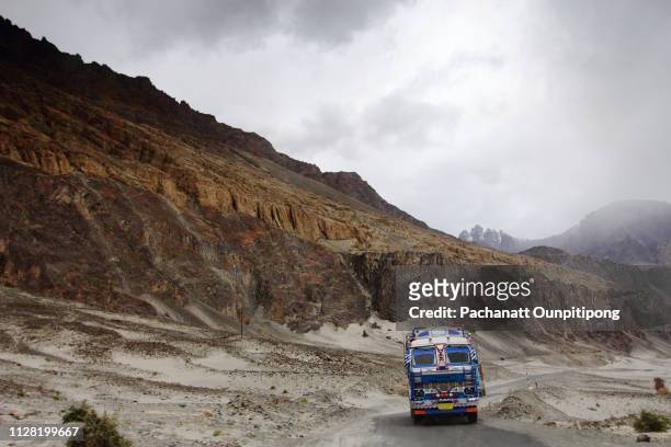 big indian truck driving on narrow road with mountain view on a cloudy day - nubra valley stock-fotos und bilder