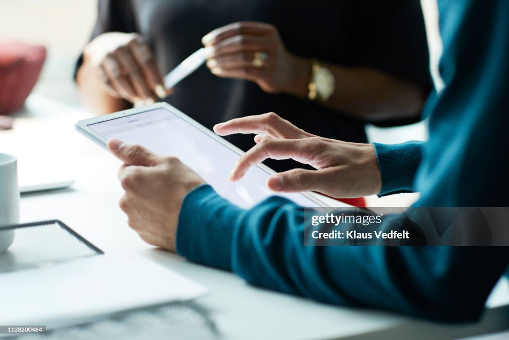 Close-up of co-workers standing at desk with laptop and talking