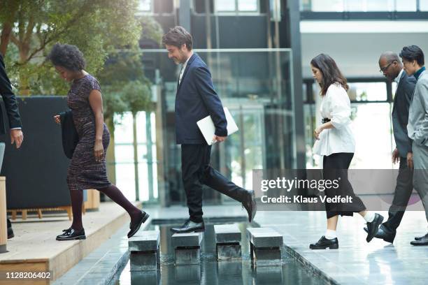 business people crossing over step stones in atrium of modern office building - coming home door stockfoto's en -beelden