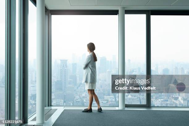 businesswoman standing in large conference room and looking out of windows - grande tablée photos et images de collection