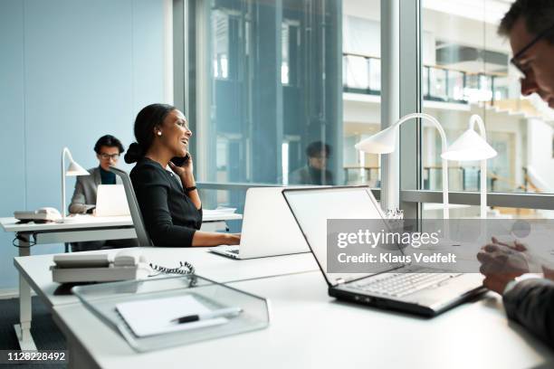 businesswoman talking on smartphone in open office - hot desking stock pictures, royalty-free photos & images