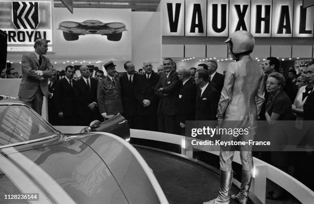 En compagnie des officiels, le général de Gaulle écoute les explications devant le stand Chevrolet où est exposée une voiture futuriste la 'Astero 2'...