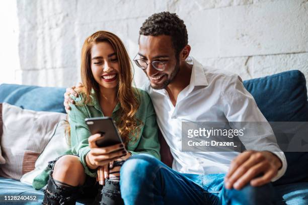 latino woman and mixed race guy are young couple, enjoying moments at home - celebrating in sofa stock pictures, royalty-free photos & images