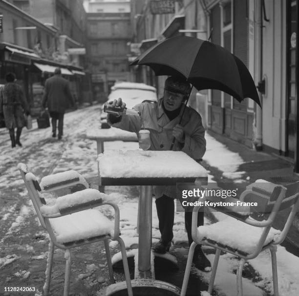Malgré la neige abondante, ce jeune Parisien, sous son parapluie, boit une bière à la terrasse d'un café dans la Cité Berryer, à Paris, France, le 17...