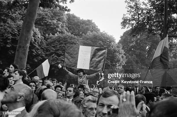 Dans la foule de manifestants, une jeune femme, juchée sur les épaules d'un camarade brandit un drapeau tricolore, à Paris, France, le 31 mai 1968.