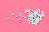 White heart shaped candies on a pink paper background. Broken heart or pearts gethering love concept.