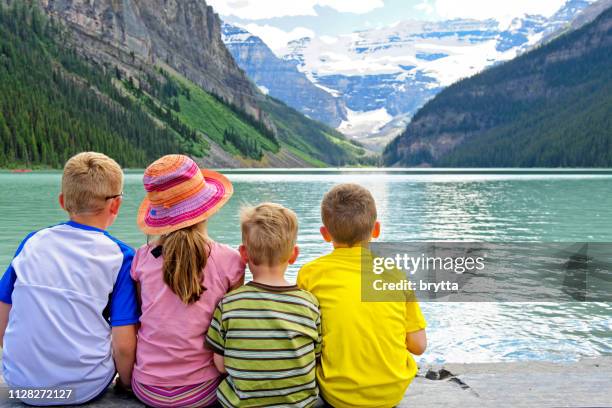 children sitting on the edge of lake louise, alberta,canada - lake louise stock pictures, royalty-free photos & images