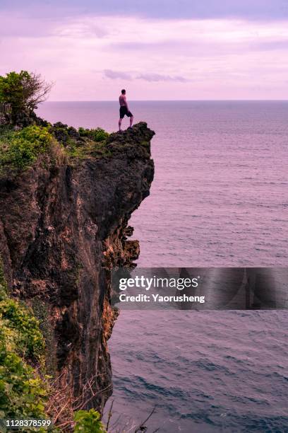 one man standing at the top over uluwatu cliff seeing the sea landscape - uluwatu stock pictures, royalty-free photos & images