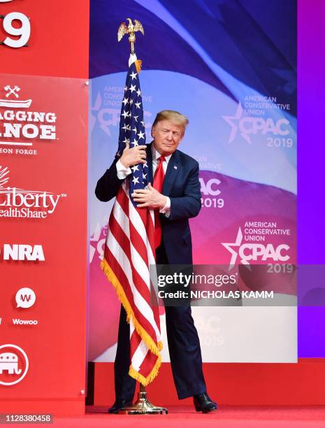 President Donald Trump hugs the US flag as he arrives to speak at the annual Conservative Political Action Conference in National Harbor, Maryland,...