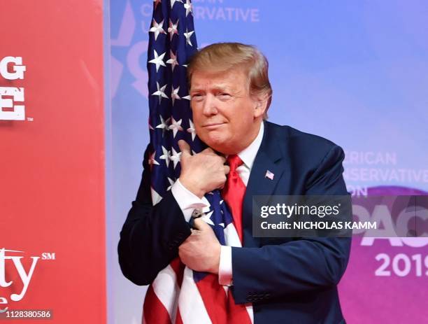 President Donald Trump hugs the US flag as he arrives to speak at the annual Conservative Political Action Conference in National Harbor, Maryland,...