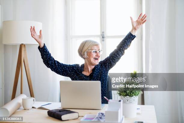 a portrait of active senior woman with laptop working in home office, expressing excitement. - stretching at work stock pictures, royalty-free photos & images