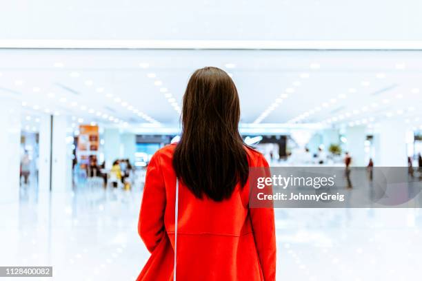 rear view of woman in red jacket in shopping mall - future retail stock pictures, royalty-free photos & images