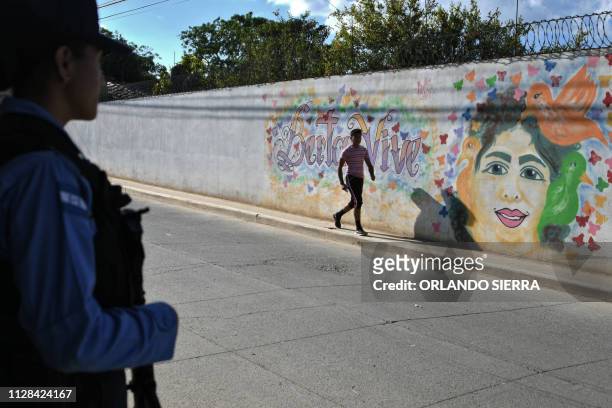 Police officer stands guard as a man walks past a mural reading "Berta Lives", referring to Honduran late environmentalist Berta Caceres on the eve...