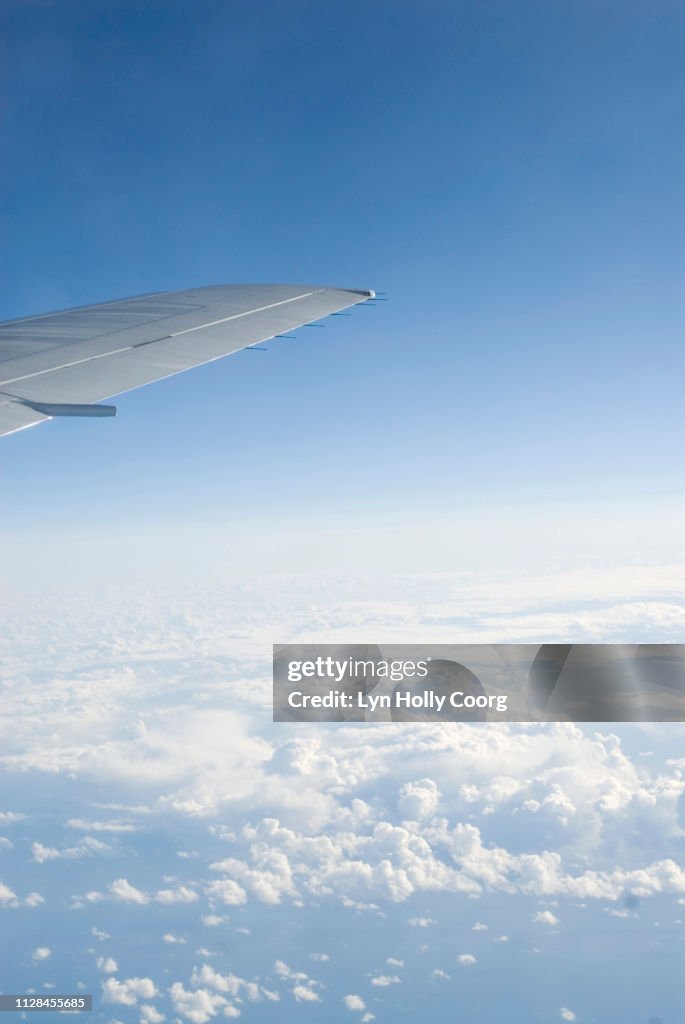 Wing tip of plane in cloudy blue sky