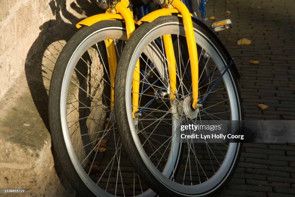 Front wheels of two yellow bicycles propped against wall