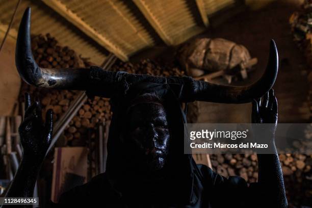 Man with his face covered in oil and soot and carrying bull horns representing a devil prepares for a traditional carnival festival. Every year Luzon...