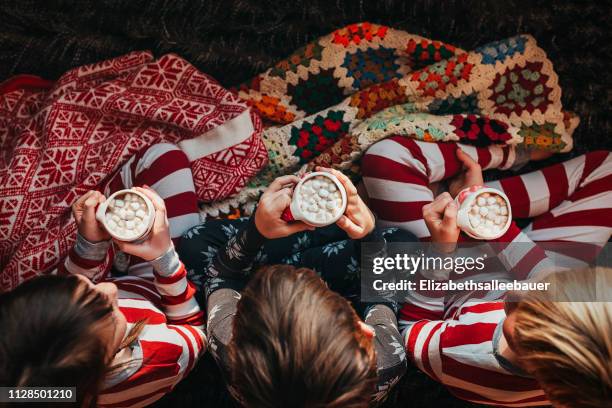 three children sitting on a couch drinking hot chocolate - marshmallow stock-fotos und bilder