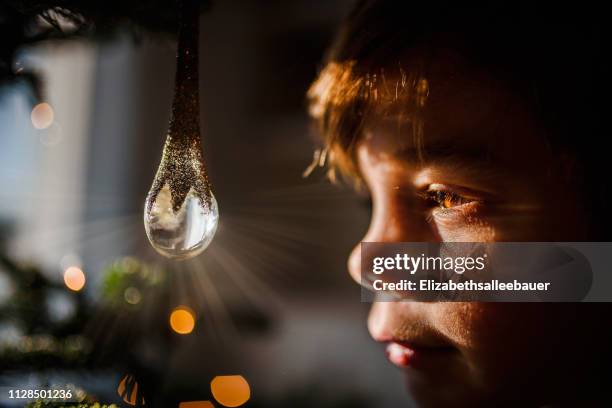 boy looking at a crystal ornament hanging on a christmas tree - magical thinking stock pictures, royalty-free photos & images