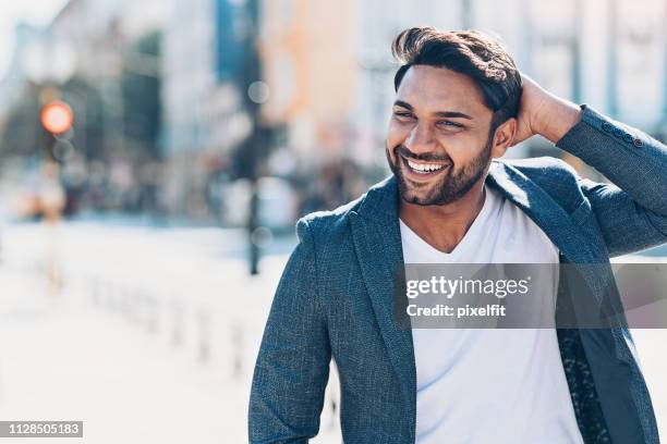 happy young indian ethnicity man on the street - hand in hair imagens e fotografias de stock