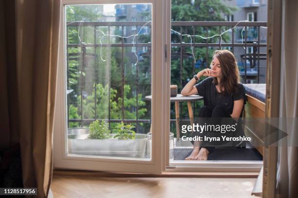 millennial girl sits on a balcony - balcony stock-fotos und bilder