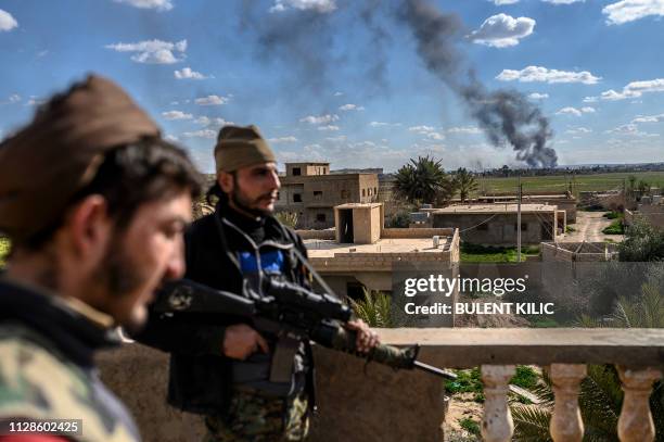 Members of the Syrian Democratic Forces stand guard on top of a building during shelling on the Islamic State group's last holdout of Baghouz, in the...