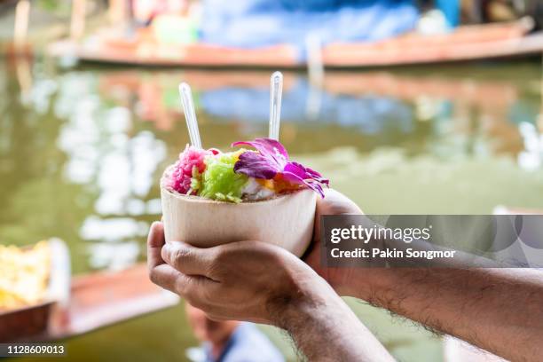 sweet coconut ice cream in the fresh coconut and plastic spoon at damnoen saduak floating market - floating market stockfoto's en -beelden