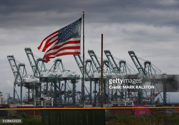 The US flag flies over shipping cranes and containers after a report said the United States and China are close to reaching a major trade deal that...