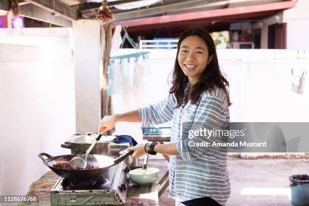 beautiful smiling thai woman cooking at home - amanda joy stock pictures, royalty-free photos & images