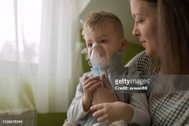 madre ayudando a pequeño hijo mediante nebulizador durante la inhalación - nebulizador fotografías e imágenes de stock