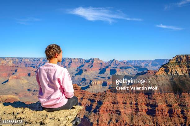 young woman looking into the distance, sitting at the precipice of the gigantic gorge of the grand canyon, view from the rim trail, between mather point and yavapai point, eroded rocky landscape, south rim, grand canyon national park, near tusayan - mather point stock pictures, royalty-free photos & images
