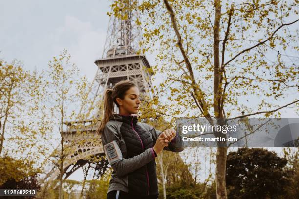 sportliche frau überprüfung puls auf smart-uhr in der nähe des eiffelturms - running paris stock-fotos und bilder