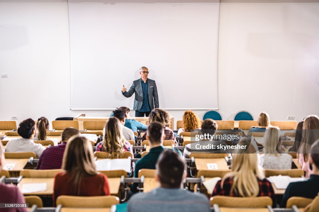 Oberlehrer im Gespräch mit großen Gruppe von College-Studenten im Amphitheater.