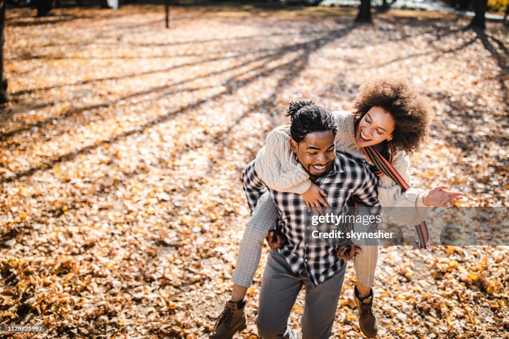 Cheerful African American couple piggybacking in autumn at the park.