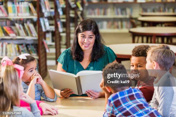 hispanic teacher reading to children in library - story stock pictures, royalty-free photos & images