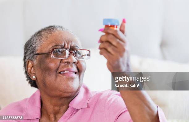 femme senior afro-américaine avec flacon de médicaments - cligner des yeux photos et images de collection