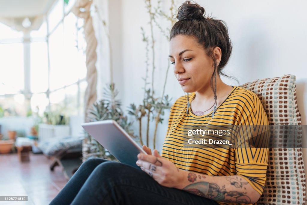 Tattooed Latina freelancer using digital tablet
