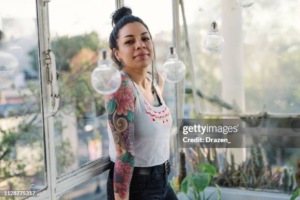 Portrait of beautiful Latina /Mexican millennial woman with tattoos near blue background