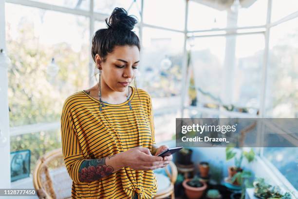 tätowierte latina mit smartphone - woman entrepreneur looking at phone stock-fotos und bilder