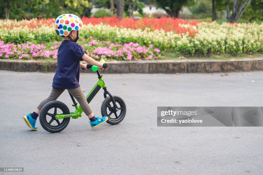 Cute little 2 - 3 years old toddler boy child wearing safety helmet learning to ride first balance bike in sunny summer day
