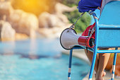 lifeguard sitting on chair with megaphone at poolside for guarding lives