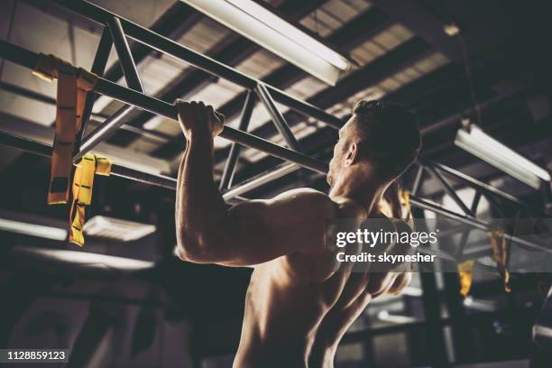 vista trasera del hombre deportivo ejercicio de dominadas en un gimnasio. - flexión de brazos fotografías e imágenes de stock