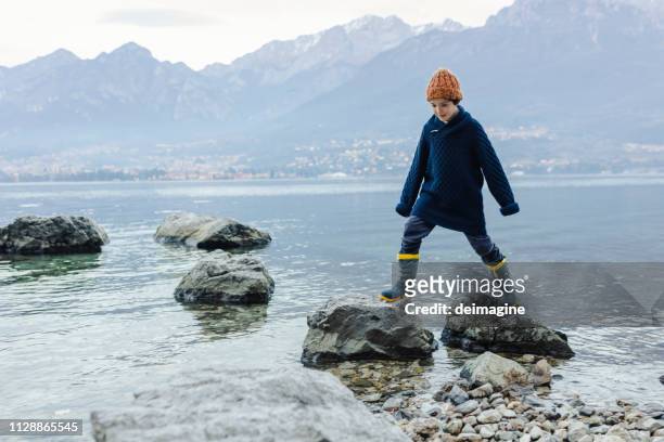 boy playing on stones on the shore of the lake - lakeshore stock pictures, royalty-free photos & images