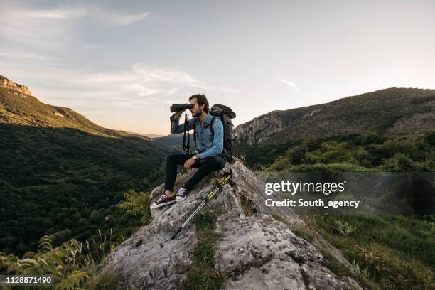 wandelaar zittend op rock op zoek door middel van verrekijkers - ergens doorheen kijken stockfoto's en -beelden