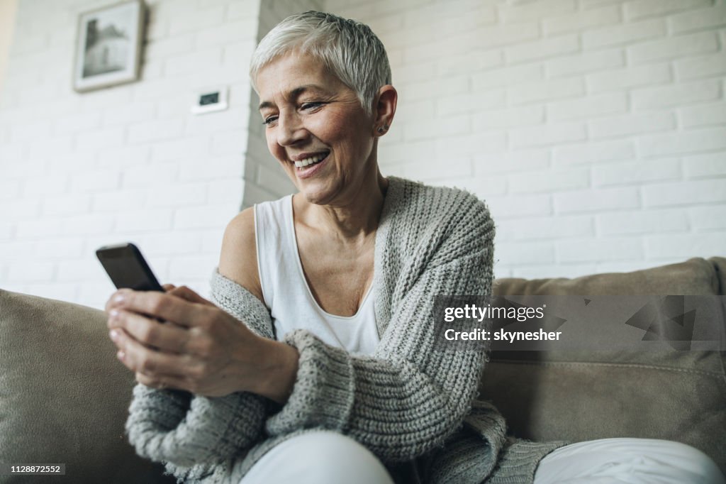 Below view of happy mature woman text messaging on mobile phone.