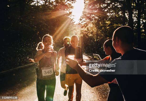 marathonläufer unter wasser von freiwilligen während eines rennens bei sonnenuntergang. - marathon stock-fotos und bilder