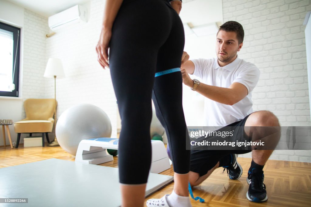 Measuring woman's circumference of leg in gym