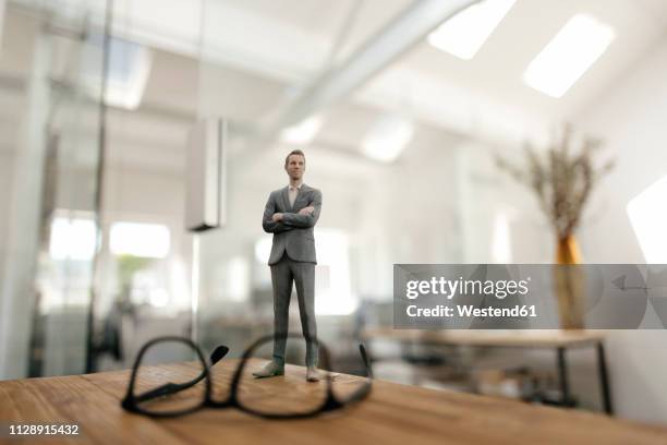 businessman figurine standing behind glasses on desk in modern office - glass figurine stock pictures, royalty-free photos & images