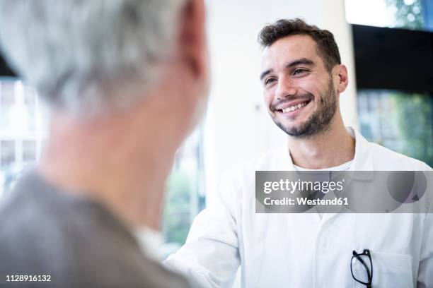 man in doctor's overall smiling at grey-haired man - arzt konsultation stock-fotos und bilder