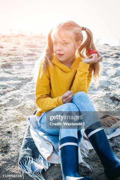 portrait of girl with plaits sitting on the beach in autumn eating an apple - eating brown bread stock pictures, royalty-free photos & images